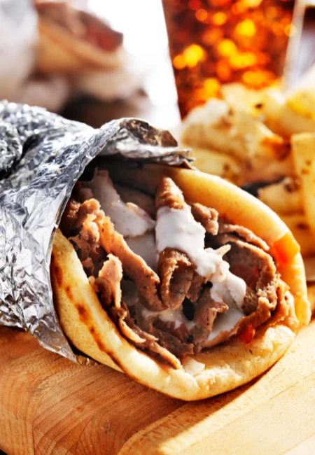 Beef gyro wrapped in aluminum foil, filled with tender beef, fresh vegetables, and creamy sauce.